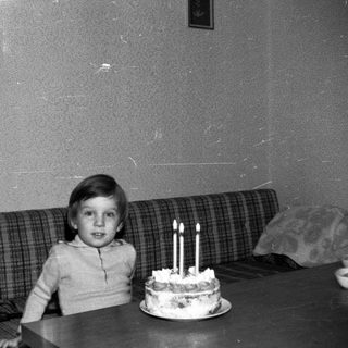 Young child sitting with birthday cake and lit candles.
