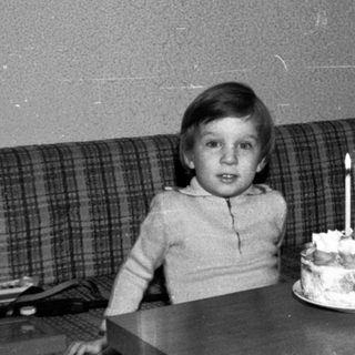 Young child sitting with birthday cake and lit candles.
