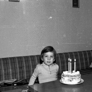 Young child sitting with birthday cake and lit candles.
