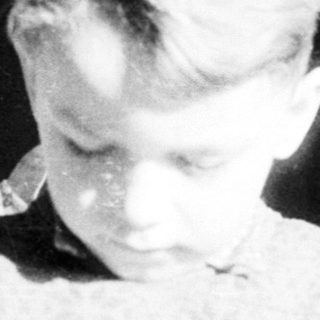 Young child sitting indoors, looking downward.