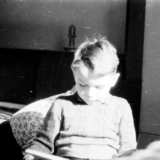 Young child sitting indoors, looking downward.