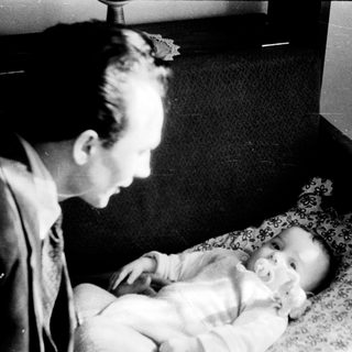 A man tenderly holds a sleeping baby indoors.