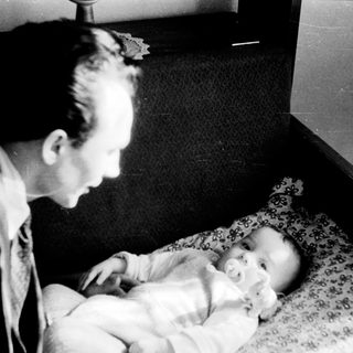 A man tenderly holds a sleeping baby indoors.