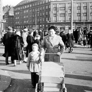 Crowded urban street scene with family pushing stroller, mid-20th century.