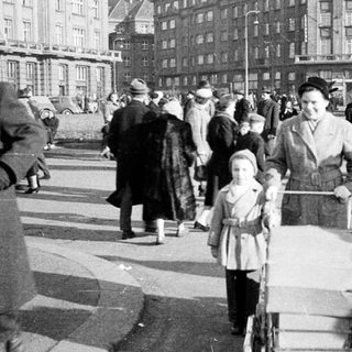 Crowded urban street scene with family pushing stroller, mid-20th century.