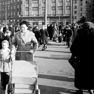 Crowded urban street scene with family pushing stroller, mid-20th century.