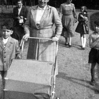 Family walking outdoors with baby stroller, mid-20th century.