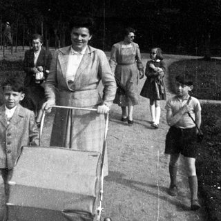 Family walking outdoors with baby stroller, mid-20th century.
