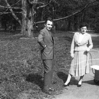 Couple pushing baby stroller in wooded area.