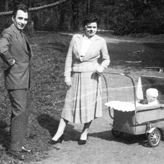 Couple pushing baby stroller in wooded area.