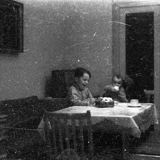 Two children eating at a small table indoors.
