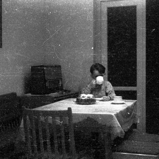 Child drinking tea at a small table indoors.