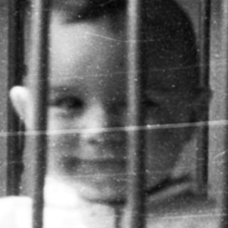 Child giving thumbs-up from inside crib.
