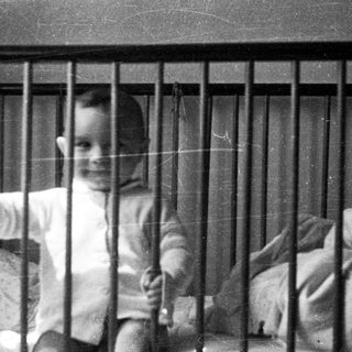 Child giving thumbs-up from inside crib.