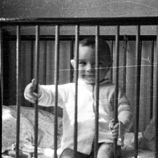 Child giving thumbs-up from inside crib.