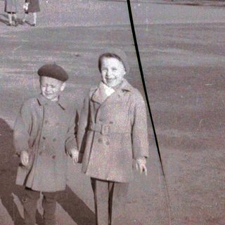 Two children posing together outdoors in vintage clothing.
