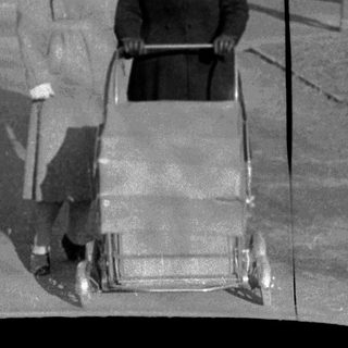 Two women pushing a baby stroller outdoors in urban setting.