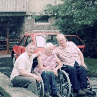 Family posing outside residential building with wheelchair.