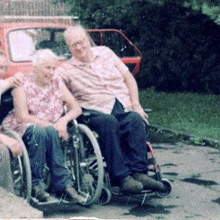 Family posing outside residential building with wheelchair.
