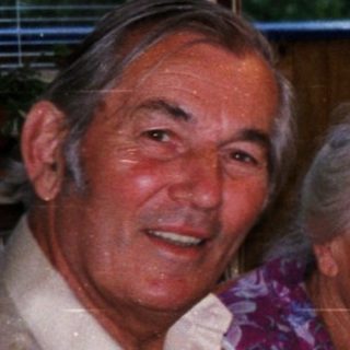 Four elderly people smiling indoors near kitchen window.