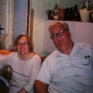 Four elderly people smiling indoors near kitchen window.