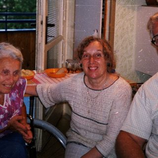 Four elderly people smiling indoors near kitchen window.