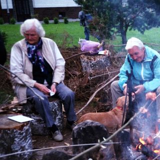 Group cooking s'mores and skewers over campfire.