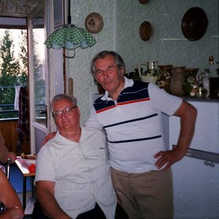 Four people posing indoors near kitchen window.