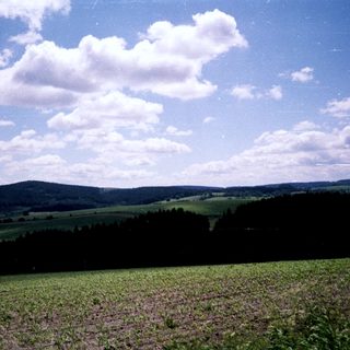 Rural countryside with fields, hills, and blue sky.