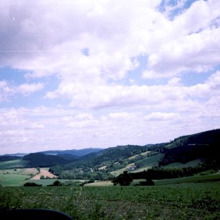 Rural landscape with rolling hills, fields, and scattered trees under blue sky.