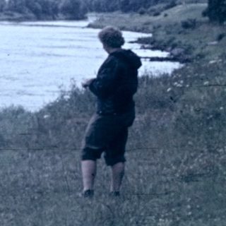Person fishing by a wide river.