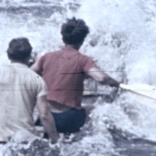Two people wading in fast-flowing water near dam spillway.