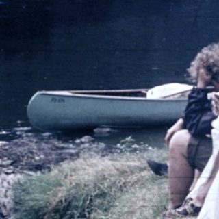 People relaxing by a lake with a canoe.