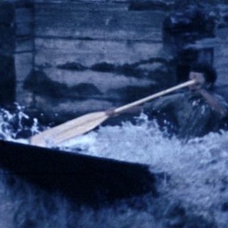 Small boat navigating turbulent river near wooden dam.