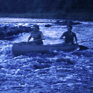 Two people paddling a canoe on turbulent river at night.