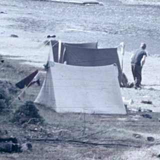 Vintage camping scene by river with tents and people.