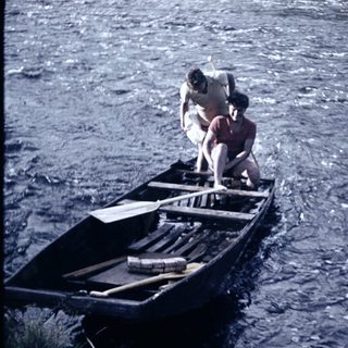 Two people paddling a wooden canoe on water.