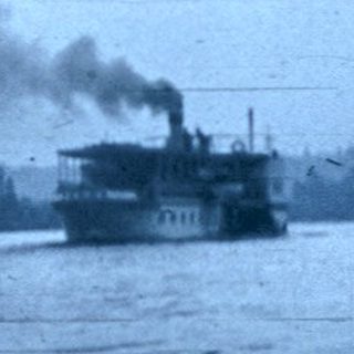 Steamship emitting smoke on a river near industrial shoreline.