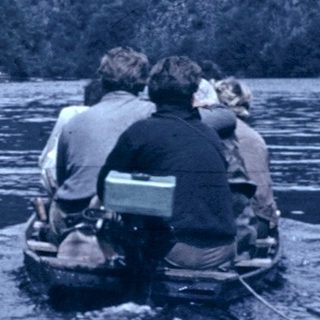 Two divers entering water near rocky coastline.
