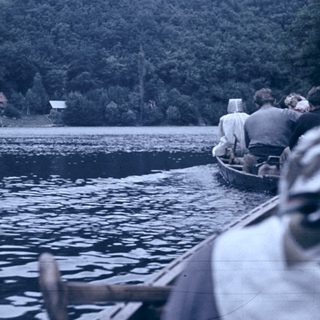 Boaters on calm lake with forested hills.
