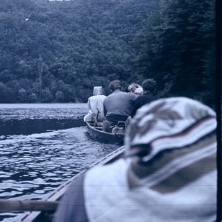 Boaters on calm lake with forested hills.