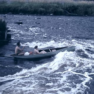 Two people rowing a small boat on turbulent water.