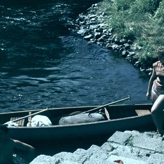 Person launching canoe into flowing river.