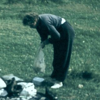 Person cleaning up discarded camping gear in grassy area.