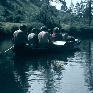 People rowing a wooden boat on calm water.