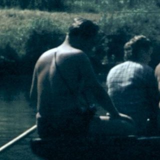 People rowing a wooden boat on calm water.