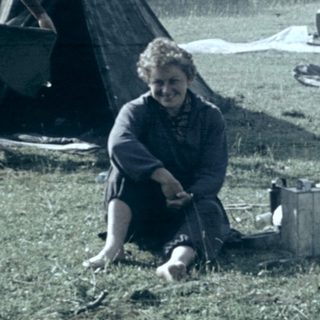 People camping outdoors with tents in grassy field.