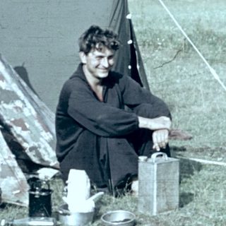 Person camping outdoors with tent and cooking setup.