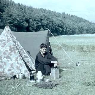 Person camping outdoors with tent and cooking setup.