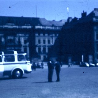 Vintage bus in urban square with pedestrians.